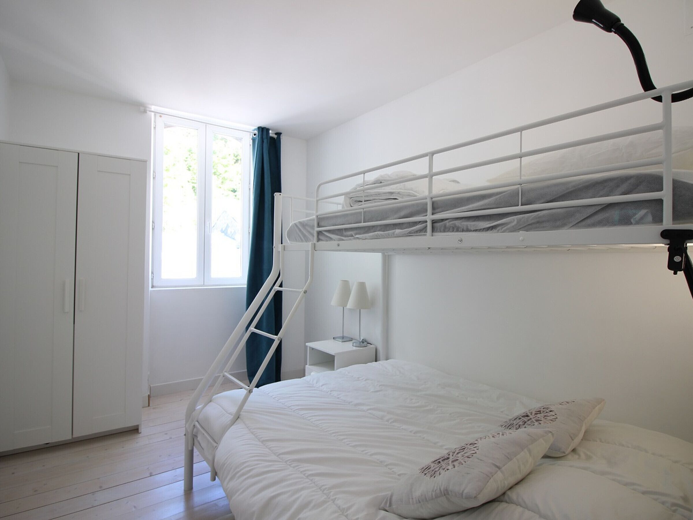 Ein Schlafraum mit Etagenbetten, einer Treppe, einem Nachttisch mit Lampe und einem Kleiderschrank.