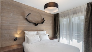 A modern bedroom with a wooden headboard, a bed with white linens, a mounted deer head decoration, and a pendant light.