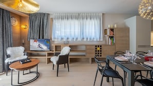 A modern living room with a TV, seating, a dining area, and a large window with curtains.