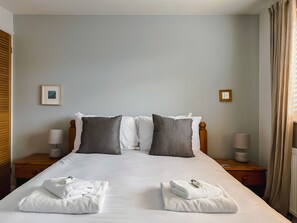 Una cama bien hecha con sábanas blancas y dos toallas dobladas al pie.