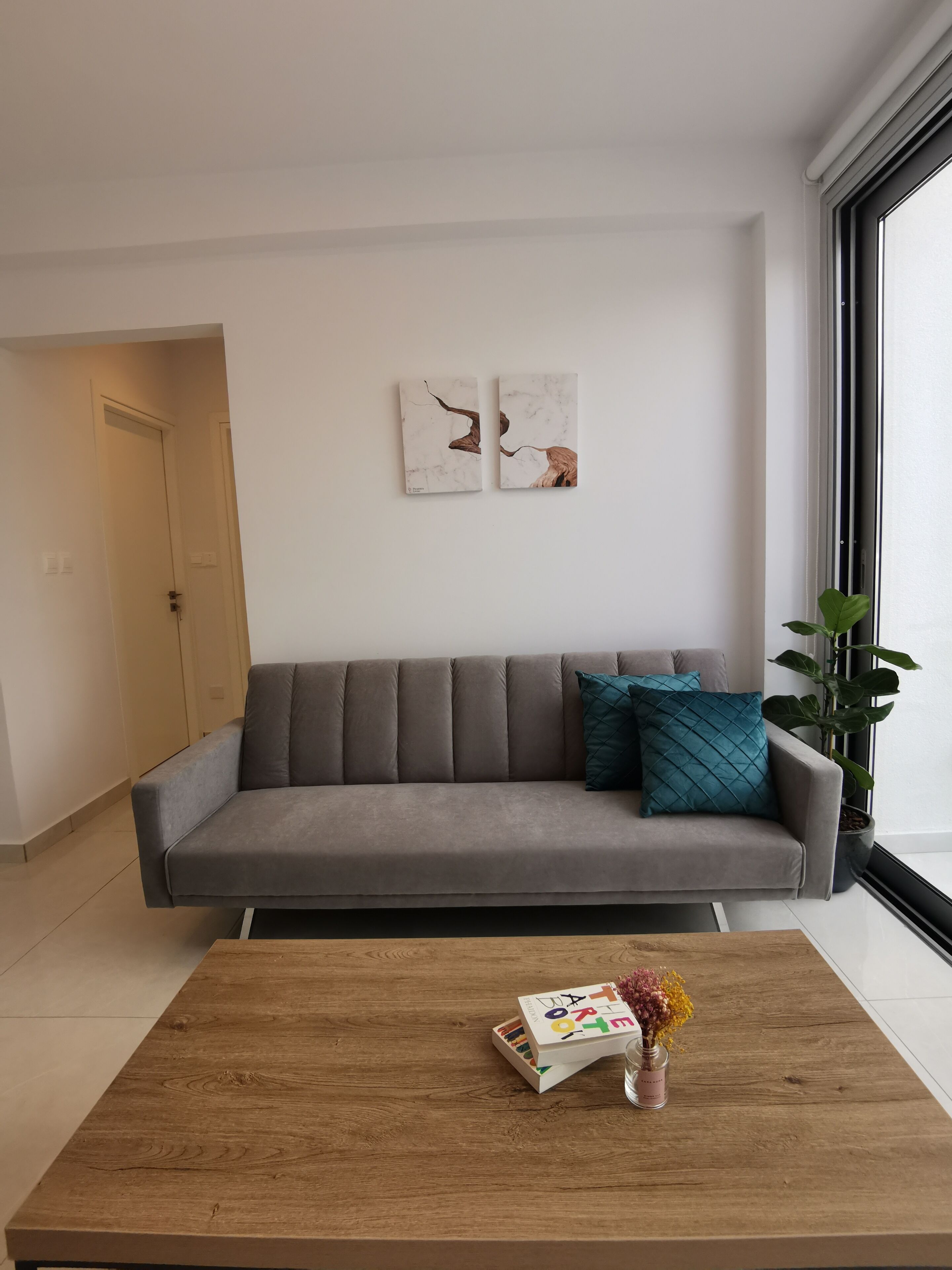 A modern living room with a grey sofa, teal pillows, and two abstract wall art pieces.
