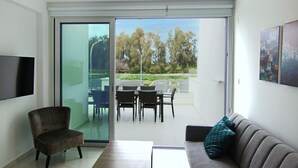 A modern living room with a sofa, a chair, a table, and a sliding glass door leading to an outdoor patio with a dining set.