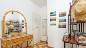 A room with a wooden dresser, a mirror, a bookshelf with books and a hat, and a wall with framed pictures. - Effie Apartment in (Corfu)