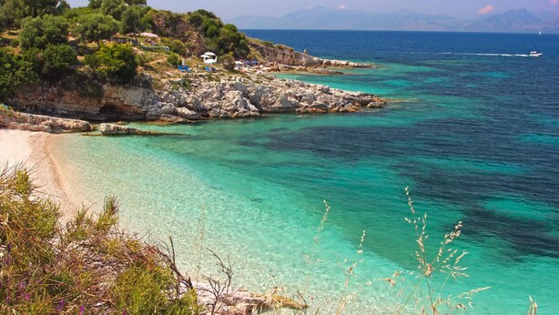 A coastal landscape with clear turquoise waters, rocky terrain, and a few buildings on the hillside. - Effie Apartment in (Corfu)