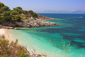 Eine Küstenlandschaft mit klarem türkisblauem Wasser, felsigem Gelände und einigen Gebäuden am Hang.