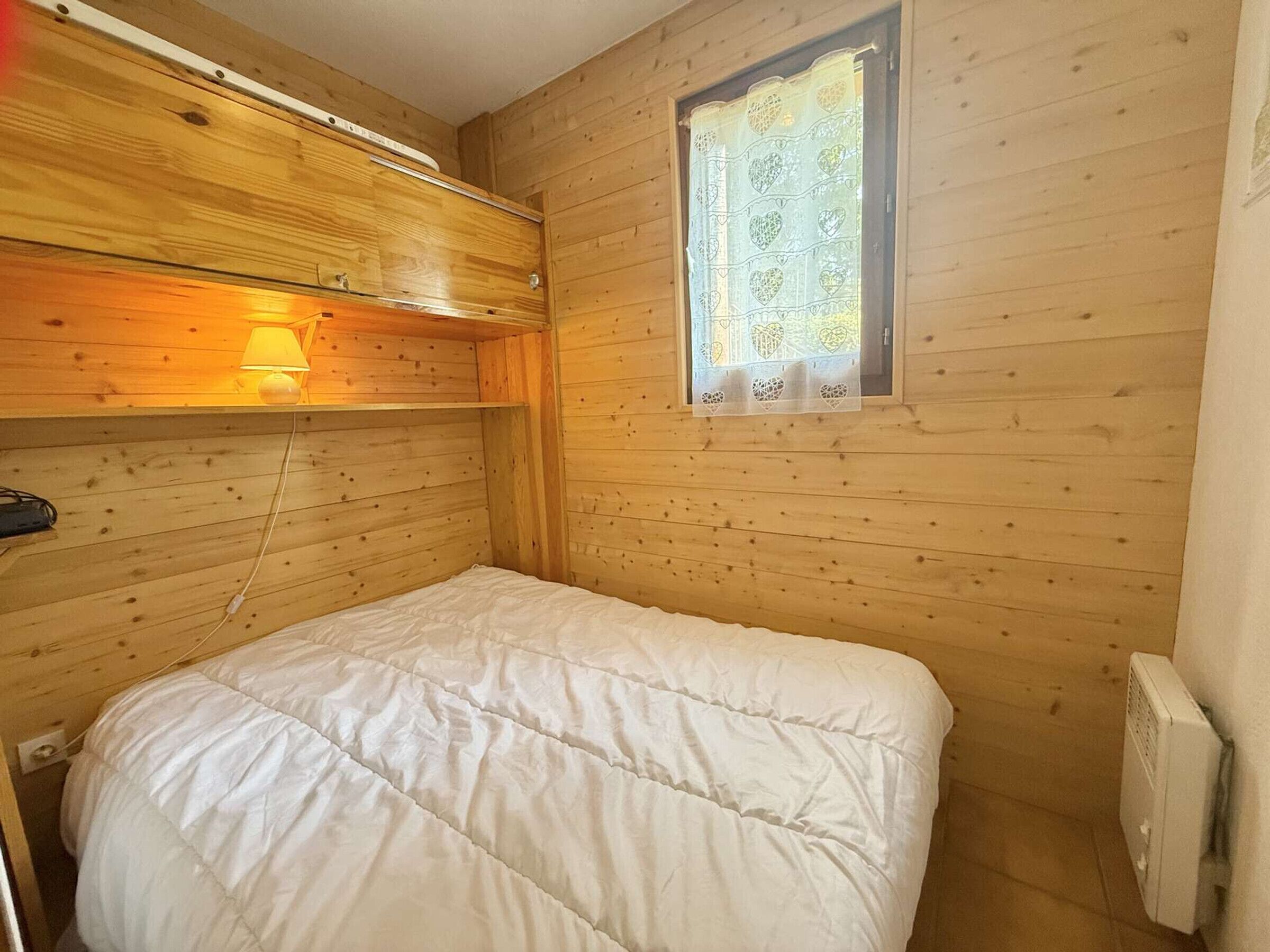 Una camera in legno con un letto, una finestra con tende a motivi floreali e un termosifone a parete.