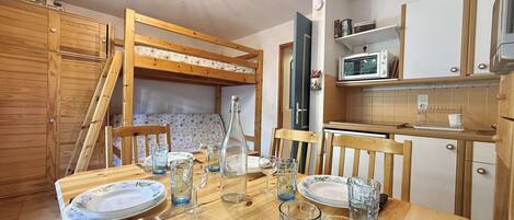 A compact kitchen with wooden cabinets, a microwave, and a dining table set with plates and glasses.