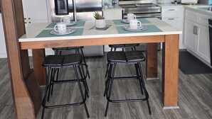 A modern kitchen with white cabinets, stainless steel appliances, and a wooden dining table with two black bar stools.