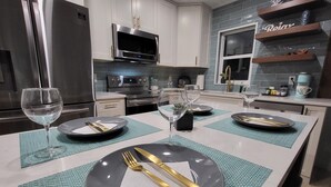 A modern kitchen with stainless steel appliances, a central island with dining setup, and a decorative shelf.