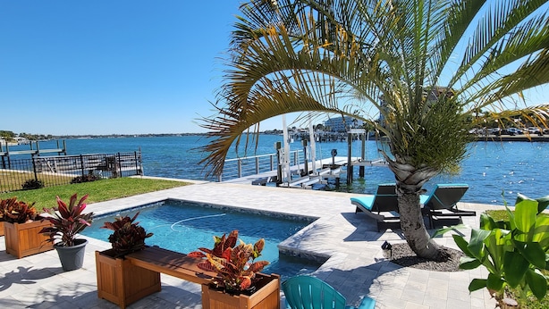 A poolside area with a view of the water, lounge chairs, and potted plants.