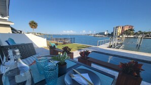A dining area with a view of the water, a table set with a bottle, glasses, and a plate, and potted plants.