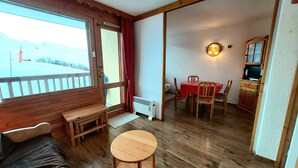 Ein Zimmer mit einer Holzbank, einem kleinen runden Tisch, einem Esstisch mit Stühlen, einem Heizkörper und einem Fernseher in einem Holzschrank.