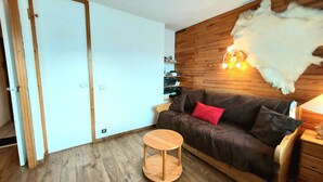 Ein Zimmer mit einem braunen Sofa, einem runden Holztisch, einem weißen Fellteppich und Holzwandverkleidungen.