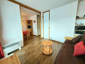 Uma sala de estar com um sofá marrom, uma mesa de centro redonda de madeira e uma mesa vermelha com cadeiras.