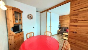 Ein Essbereich mit einem roten Tisch, Holzstühlen, einem Fernseher auf einer Holzkommode und einer Uhr an der Wand.