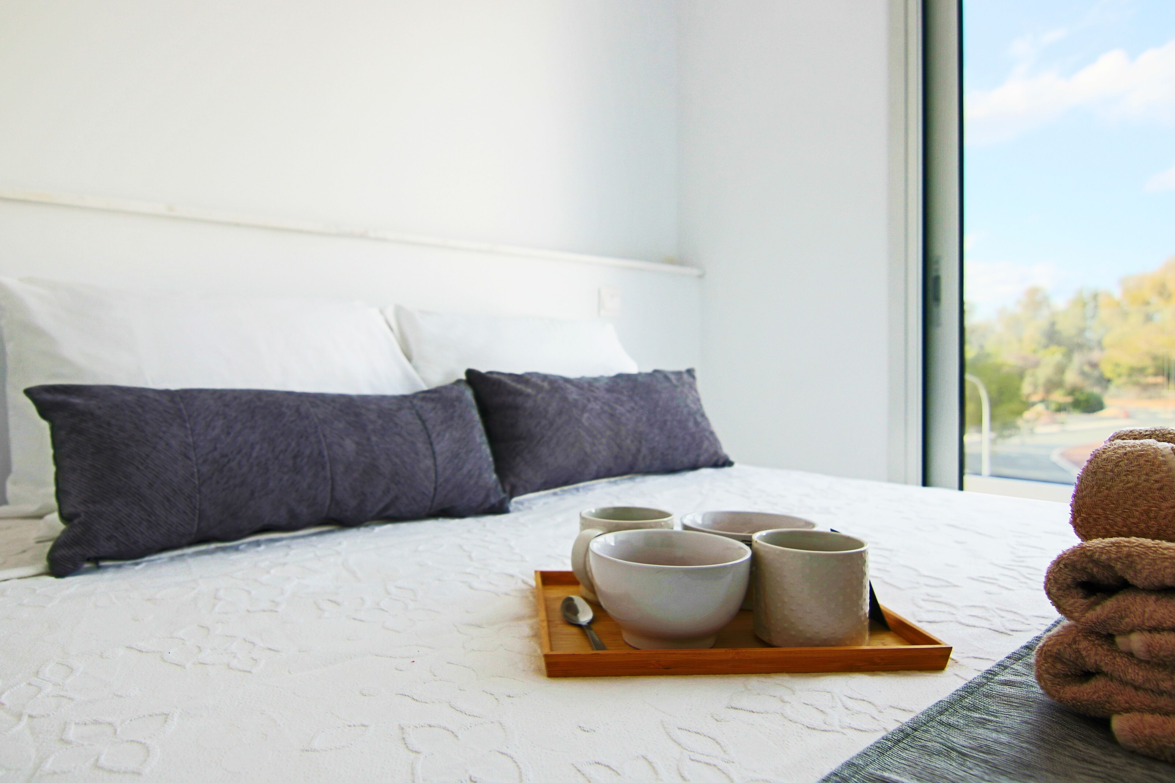 A neatly made bed with pillows, a tray with bowls and a spoon, and a teddy bear on the right.