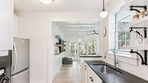 A modern kitchen with white cabinetry, a black countertop, and a window with a view of the outdoors. - Renovated Cottage w/New Heated Swimming Pool at East Beach's 6th St. Access (Saint Simons Island)