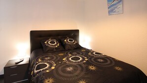 Une chambre à coucher avec une couvre-lit marron foncé ornée de motifs circulaires, une table de chevet avec une télécommande et un tableau accroché au mur.