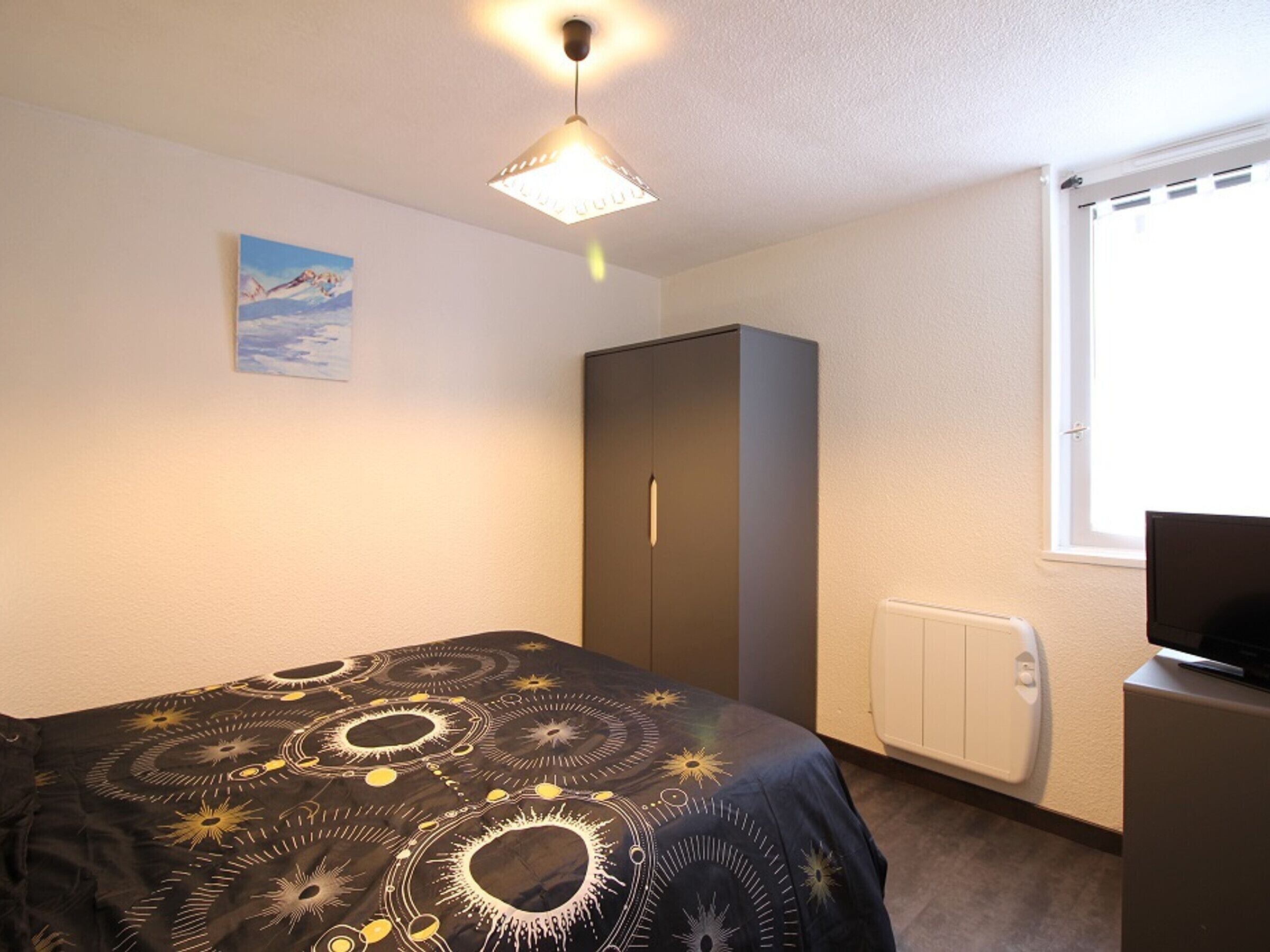 Ein Schlafzimmer mit Bett, Kleiderschrank, Heizkörper und Fernseher auf einem Schrank.