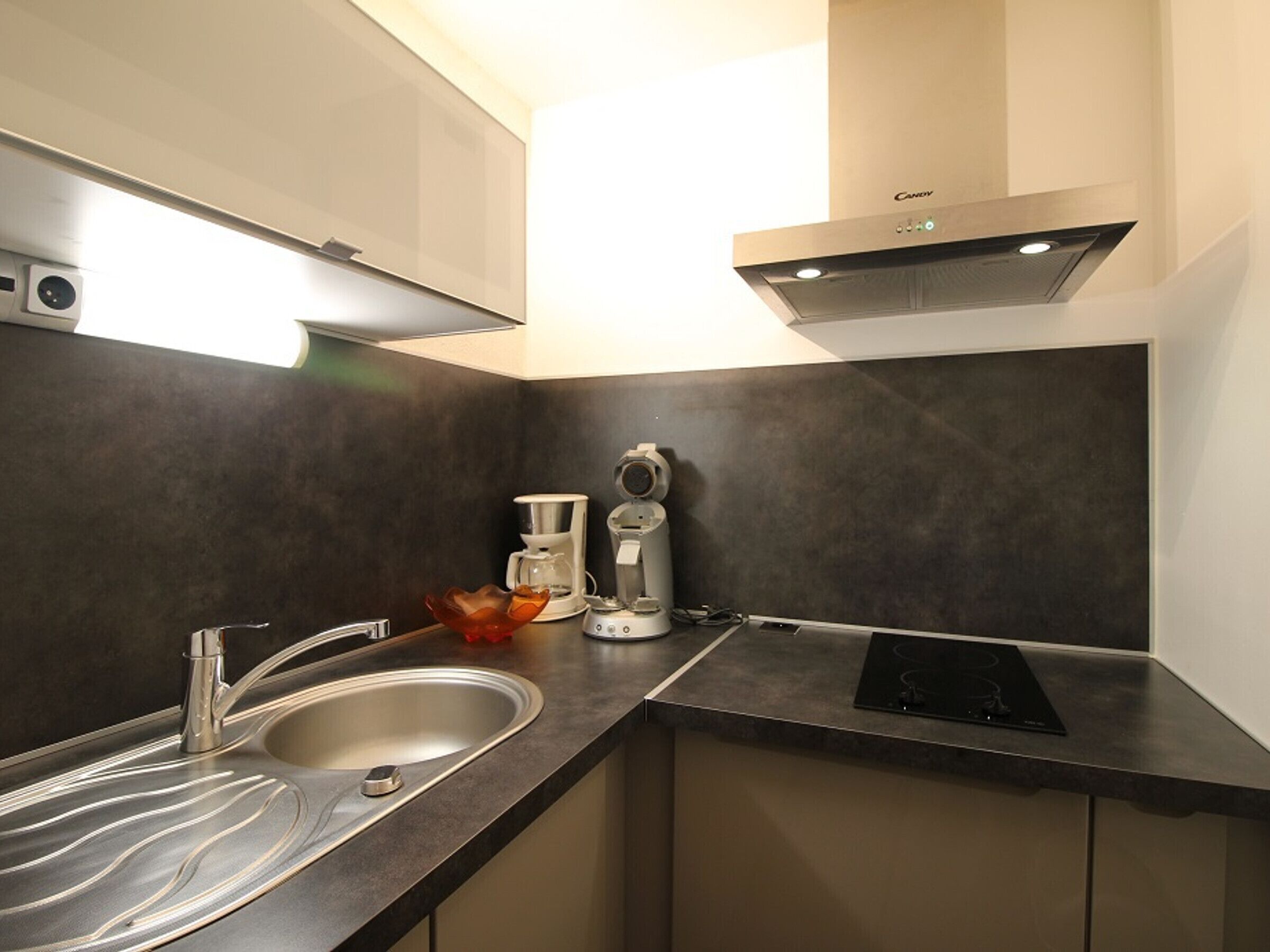 A modern kitchen with a stainless steel sink, a coffee maker, and a built-in range hood.