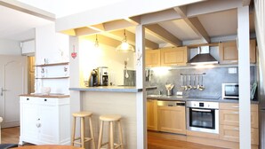 A modern kitchen with wooden cabinets, stainless steel appliances, and a bar area with stools. - Cozy T2 bis with Wi-Fi, 100m from center, sleeps 6, ski & bike storage (Mont-Dore)