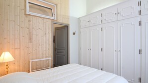 A bedroom with a bed, a wooden wall, a white wardrobe, and a door. - Cozy T2 bis with Wi-Fi, 100m from center, sleeps 6, ski & bike storage (Mont-Dore)