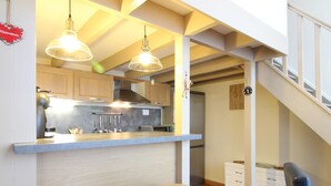 A modern kitchen with wooden cabinets, a bar area with stools, and a staircase leading to an upper level. - Cozy T2 bis with Wi-Fi, 100m from center, sleeps 6, ski & bike storage (Mont-Dore)