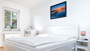 Ein modernes Schlafzimmer mit einem großen Bett, Nachttischen, einem Fenster mit Blick und einem gerahmten Bild an der Wand.