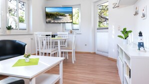 Ein modernes Wohnzimmer mit einem Flachbildfernseher, weißen Möbeln und Holzboden.
