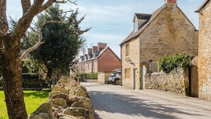 Un bâtiment en pierre avec un toit à deux versants et une cheminée, situé dans une rue tranquille où une voiture est garée.