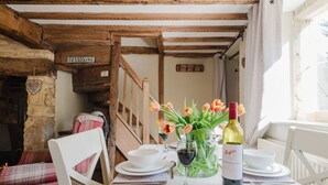 Un coin repas rustique avec des poutres en bois, un panneau indiquant «Il est interdit de fumer», une décoration en forme de cœur et une table dressée pour deux personnes, avec des assiettes, des verres et une bouteille de vin.