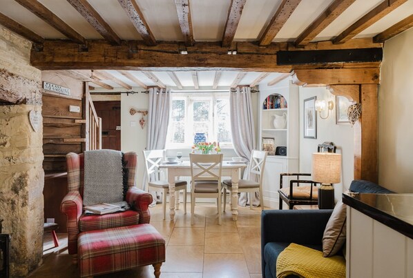 A rustic interior with exposed wooden beams, a dining area with a table and chairs, and a cozy seating area with a sofa and armchair. - A beautifully presented two bedroom Cotswold stone cottage in the Cotswolds - Cobblers Cottage, More (Moreton-in-Marsh)