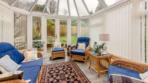 A conservatory with wicker furniture, a patterned rug, and a lamp. - Beautiful three bedroom family friendly Costwold holiday cottage - Rose Tree Cottage,  Stroud (Stroud)