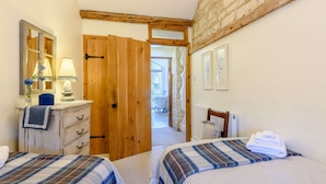 A bedroom with two beds, a dresser, a mirror, and a wooden door leading to a bathroom. - Beautiful three bedroom family friendly Costwold holiday cottage - Rose Tree Cottage,  Stroud (Stroud)