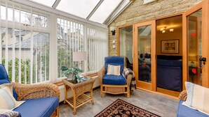 A sunroom with wicker furniture, a glass door leading outside, and a view of the garden. - Beautiful three bedroom family friendly Costwold holiday cottage - Rose Tree Cottage,  Stroud (Stroud)