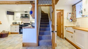 A kitchen with a central island, a microwave, stove, and various kitchen utensils. - Beautiful three bedroom family friendly Costwold holiday cottage - Rose Tree Cottage,  Stroud (Stroud)