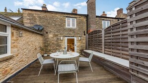 A stone building with a wooden fence, a round table with chairs, and a door leading to an interior space. - Stylish two bedroom family friendly holiday Apartment in Stow-on-the-Wold - Church View Apartment (Cheltenham)