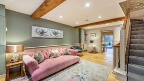 A living room with a pink sofa, a wooden floor, a ceiling with exposed beams, and a staircase. - Stylish two bedroom family friendly holiday Apartment in Stow-on-the-Wold - Church View Apartment (Cheltenham)
