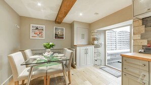 A modern kitchen with white cabinets, a glass dining table, and a view of the city through a large window. - Stylish two bedroom family friendly holiday Apartment in Stow-on-the-Wold - Church View Apartment (Cheltenham)