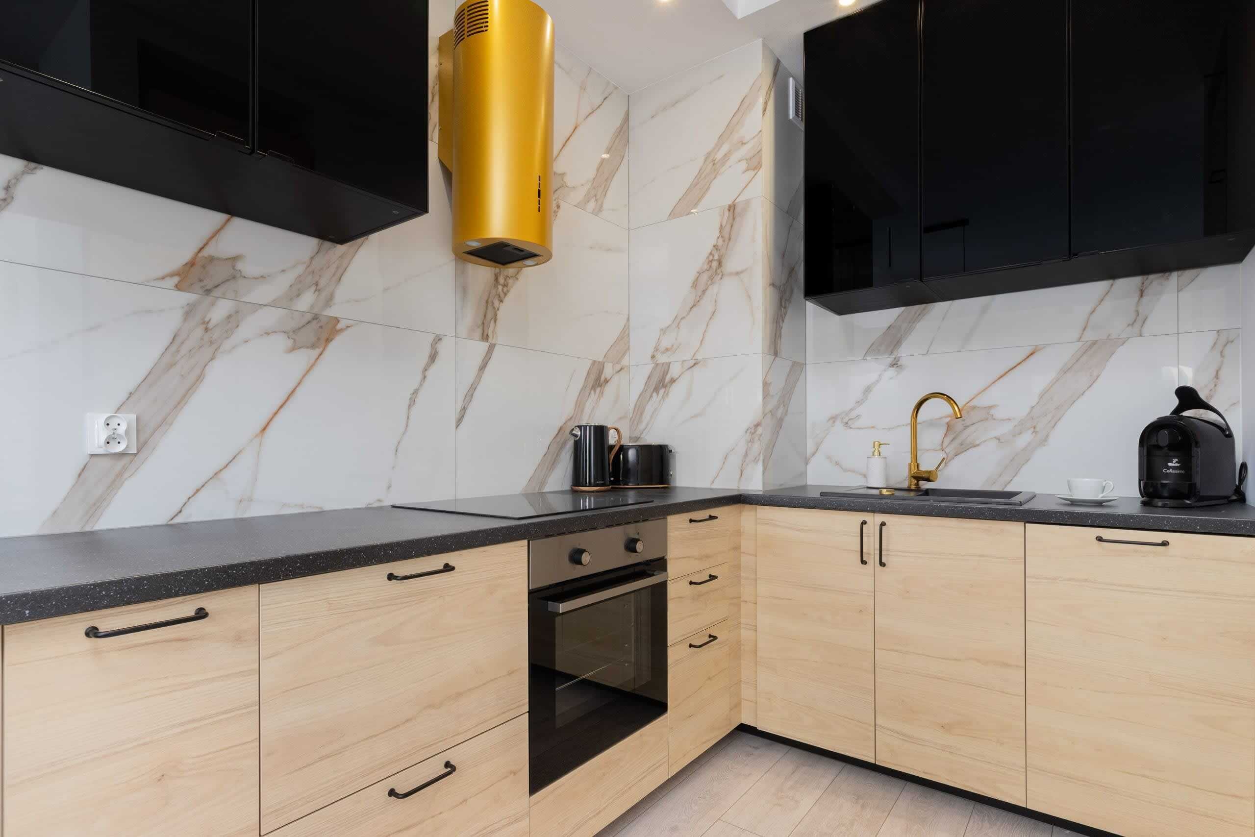 A modern kitchen with marble backsplash, black cabinets, and a gold range hood.
