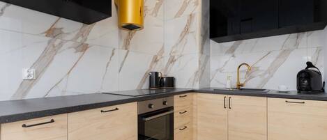 A modern kitchen with marble backsplash, black cabinets, and a gold range hood.