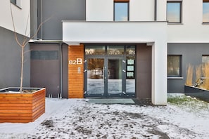 Un bâtiment moderne doté d’un jardinier en bois, d’une entrée avec une porte en verre et d’une enseigne indiquant « 82B ».