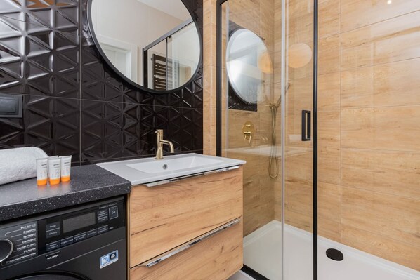 Ein modernes Badezimmer mit einer schwarzen, geometrisch gemusterten Wand, einem weißen Waschbecken und einer Duschkabine aus Glas.
