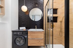 A modern bathroom with a washing machine, a sink, and a shower.