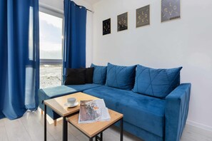 A room with a blue sofa, a wooden table with a cup and a magazine, and a window with blue curtains.