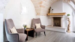 A room with two armchairs, a small table with a vase, a fireplace, and a stone wall. - Charming apartment on several levels, located in a renovated period building, of which it retains fascinating evidence in the internal architecture. The flat is ideally located, outside the ZTL but a few steps from the historic center of Ostuni, in an ar (Ostuni)