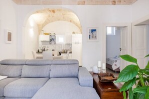 Ein Wohnzimmer mit grauem Sofa, einem Holztisch und einer großen Pflanze.