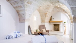 A room with a stone ceiling, a bed with rolled towels, a chair, a small table with a plant, and a fireplace. - Charming apartment on several levels, located in a renovated period building, of which it retains fascinating evidence in the internal architecture. The flat is ideally located, outside the ZTL but a few steps from the historic center of Ostuni, in an ar (Ostuni)