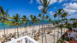 A beach view with palm trees, a clear sky, and a building with a red roof. - Punta Cana Condo for Rent (Punta Cana)
