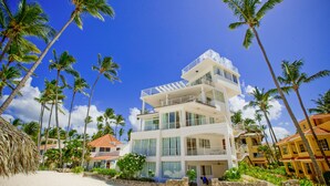 A multi-story hotel with balconies, located on a beach with palm trees. - Punta Cana Condo for Rent (Punta Cana)